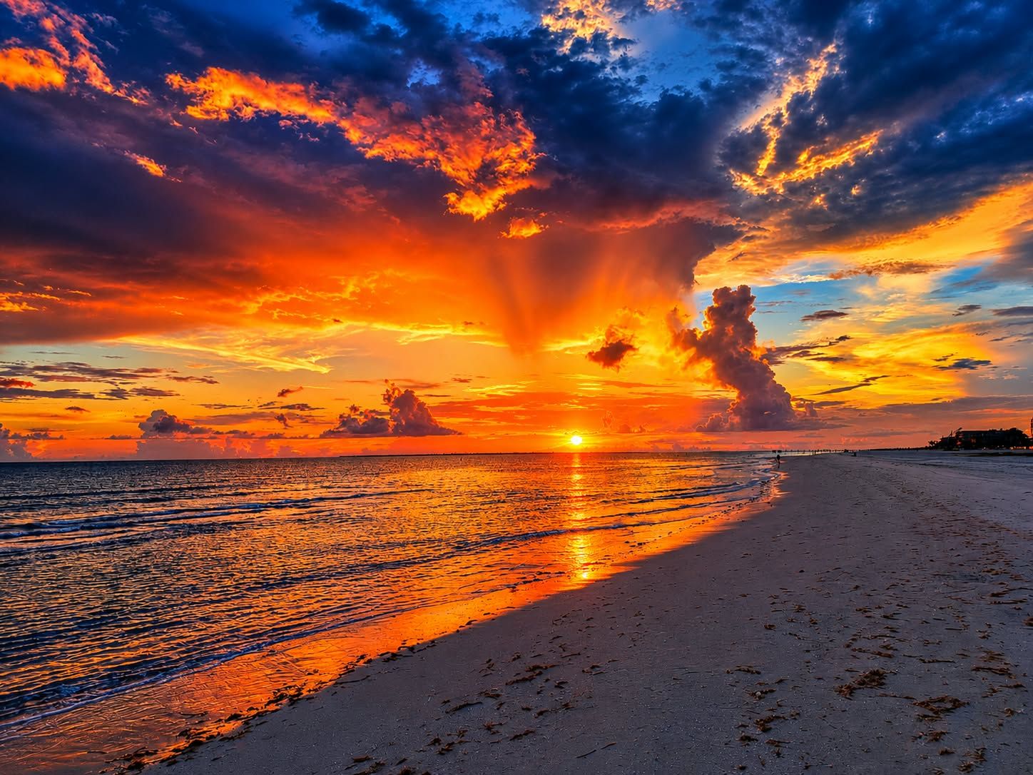 A beach with a sunset, clear sky, and calm sea.