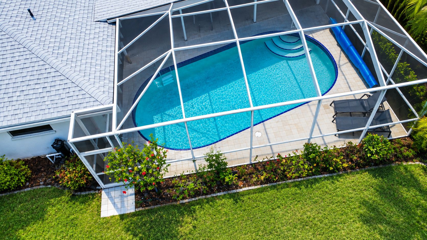 A rooftop swimming pool with a glass enclosure, surrounded by a well-maintained lawn and a white building.