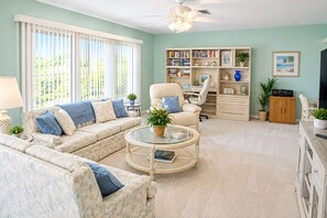 A living room with a sofa, armchair, coffee table, bookshelf, and a television.