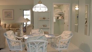 Un salón con un comedor de mimbre blanco, una lámpara colgante y un sofá blanco.