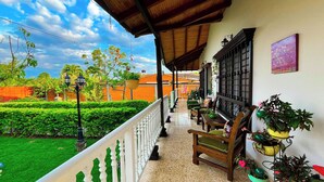 Ein überdachter Balkon mit Blick auf einen gepflegten Garten, einer hölzernen Bank und einem Blumentopf.