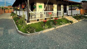 Ein zweistöckiges Gebäude mit einem Ziegeldach, einem Balkon mit weißen Geländern und einem Garten mit verschiedenen Pflanzen und Blumen.