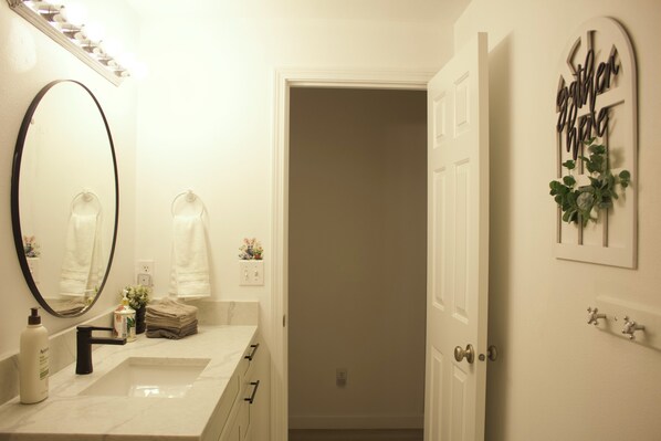 A bathroom with a large mirror, a sink, and a towel rack. There is a door leading to another room. - Backstage at Ridgefield (Ridgefield)