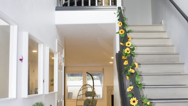 A staircase with a railing decorated with sunflowers, a white console table with a potted plant, and a hanging chair.