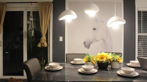 A dining area with a marble table, white plates, bowls, and a vase of sunflowers. There are three pendant lights hanging above the table.