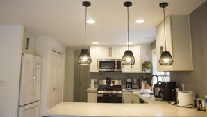 A modern kitchen with white cabinets, a stainless steel stove, and pendant lighting.
