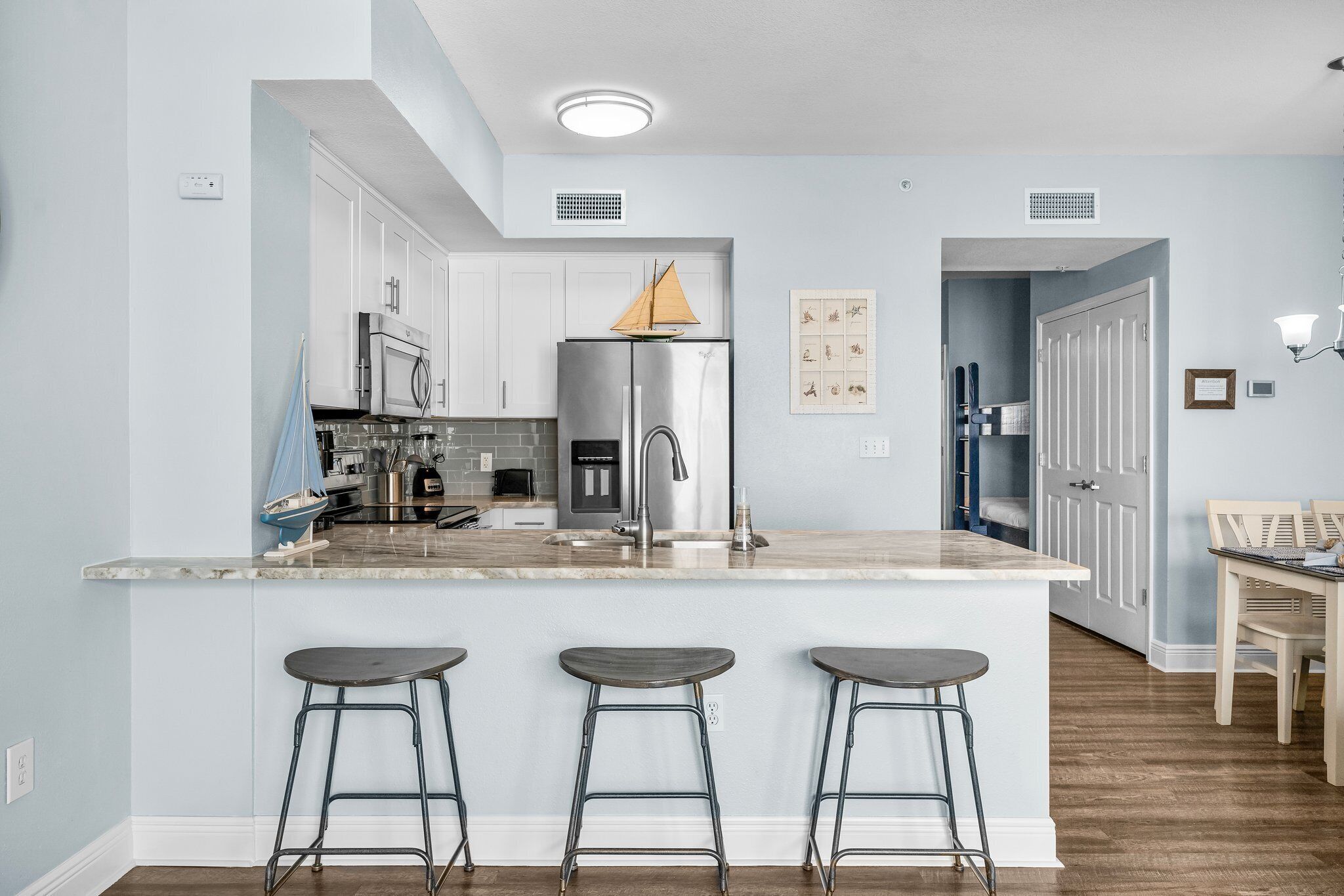 Une cuisine moderne avec des meubles blancs, des appareils en acier inoxydable, un îlot central doté de tabourets et un coin repas avec une table et des chaises.