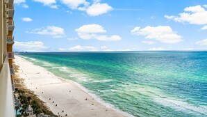 Une plage à l’eau turquoise et limpide, une rive sablonneuse et un immeuble de grande hauteur doté de balcons donnant sur la plage.