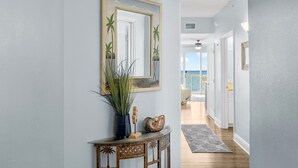 Un couloir avec un miroir, une console sur laquelle sont posés un vase et un coquillage, et une vue sur un balcon doté d’une balustrade.