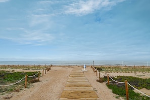 Una passerella di legno che conduce a una spiaggia, con una sedia da salvataggio blu e una recinzione lungo i lati.