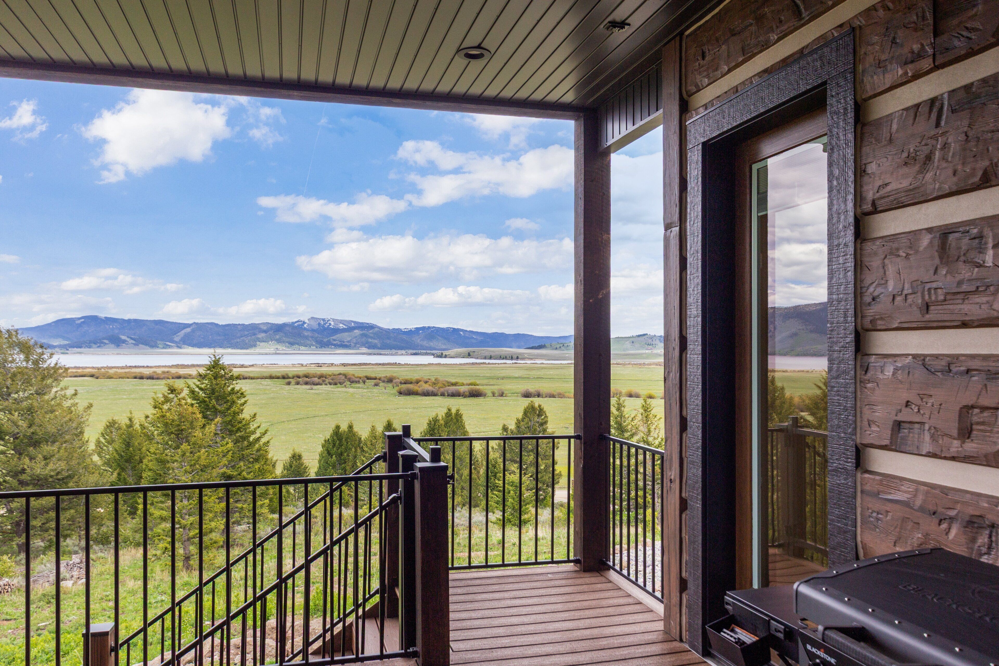 A balcony with a view of a lake and mountains, wooden railings, and a grill.