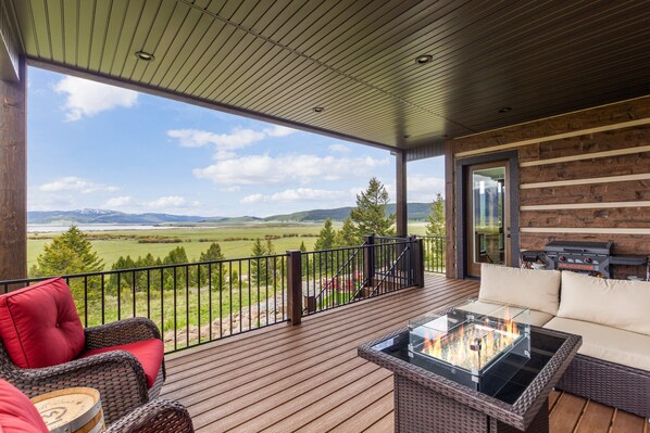 A covered deck with a glass-top table, wicker furniture, and a view of a green landscape.