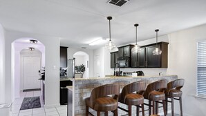 A modern kitchen with dark cabinets, a marble countertop, and pendant lighting. There are six wooden bar stools and a built-in island with a sink. - Blue Note - A Birdy Vacation Rental (San Antonio)
