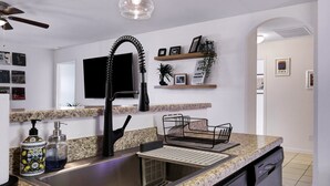 A kitchen with granite countertops, a black faucet, a dish rack, a black coffee maker, and a wall-mounted TV. - Blue Note - A Birdy Vacation Rental (San Antonio)