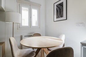 Enjoy meals in this stylish dining area with a round table and four chairs, featuring a large window and a beautiful piece of artwork.