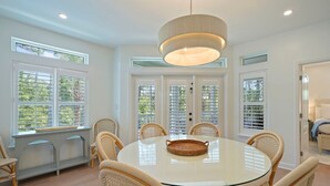 A dining area with a round glass table, wicker chairs, and a hanging light fixture.