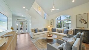 A spacious living room with a large sectional sofa, a round coffee table, and a fireplace. There are large windows providing natural light and views of the outdoors.