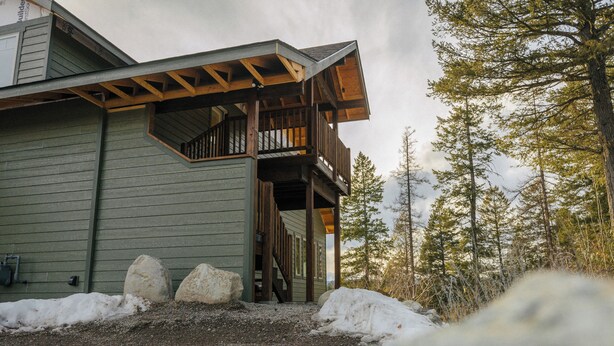 Una cabaña de madera con balcón, rodeada de nieve y árboles.
