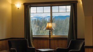 Una habitación acogedora con un ventanal grande, dos sillas, una mesita y una lámpara.