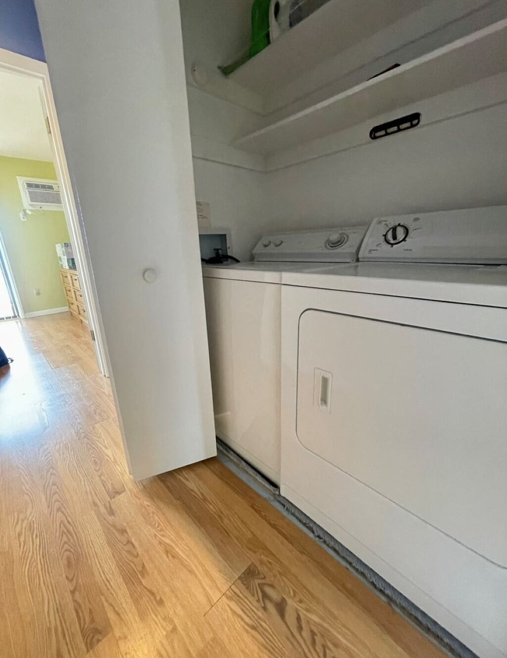 A laundry room with a washer and dryer, wooden flooring, and a door leading to another room.