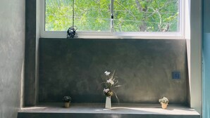 Une fenêtre donnant sur des arbres verdoyants, un luminaire suspendu et une étagère avec deux plantes en pot.