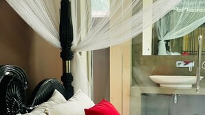 Un lit avec des oreillers blancs et rouges, une tête de lit noire et un baldaquin transparent.
