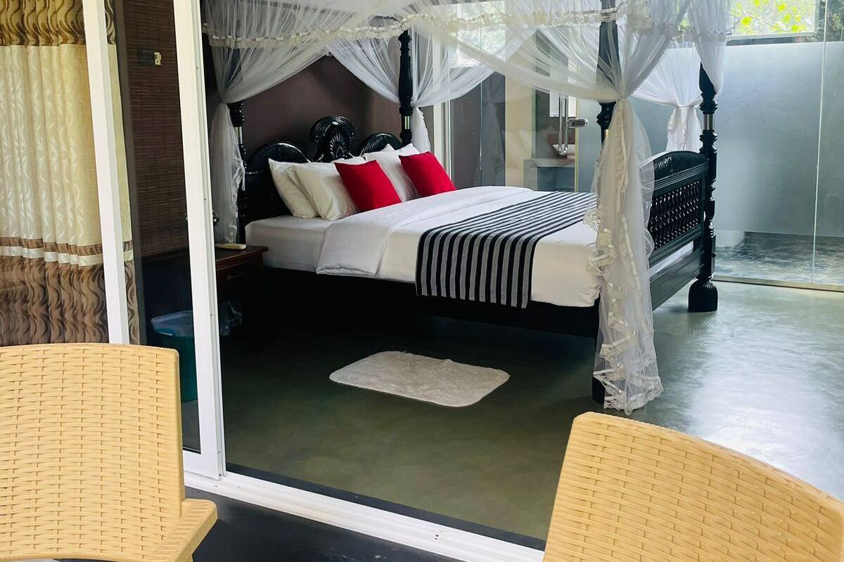 Een slaapkamer met een hemelbed en een schuifdeur naar een balkon, met rieten stoelen.