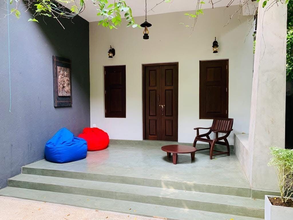 A covered outdoor area with steps leading to a door, two bean bags, a round table, and two chairs.