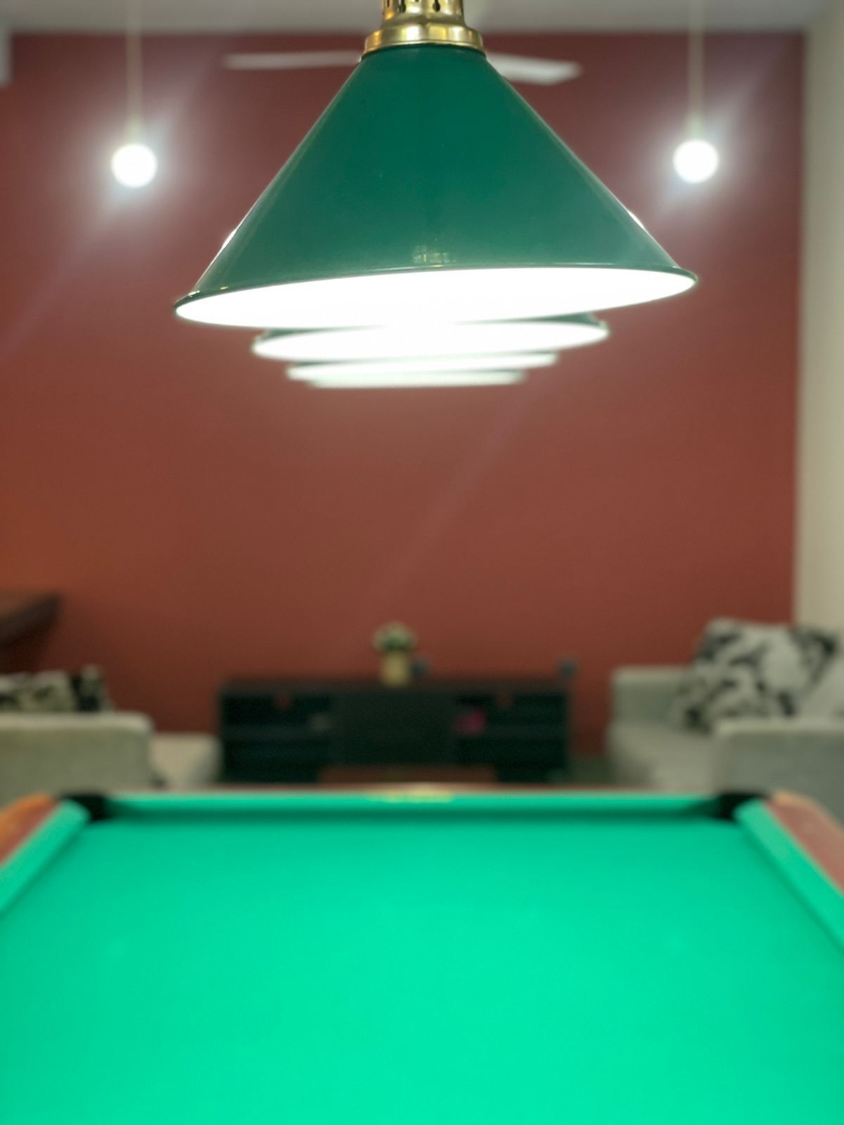 A pool table with a green felt surface and a green overhead lamp.