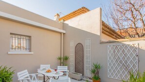 A patio with white chairs and a table, surrounded by potted plants. - Phichris by Interhome (Hyères)