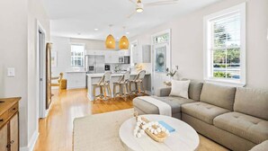 A modern kitchen with white cabinets, a dining area with wicker chairs, a beige sofa, and a ceiling fan. - Coast & Key Cottage by Stay on 30a (Seagrove Beach)
