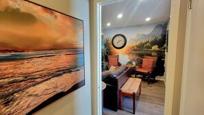 Ein Zimmer mit einem großen Gemälde einer Sonnenlandschaft, einer Wanduhr und einer Sitzecke mit einer Bank und Stühlen.