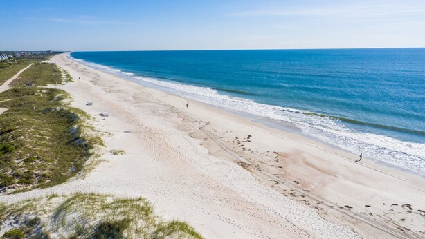 A beach with a clear sky, sandy shore, and a few people walking.