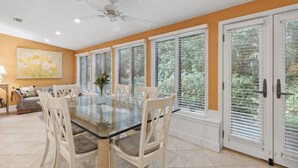 A dining area with a glass table, white chairs, and a ceiling fan.