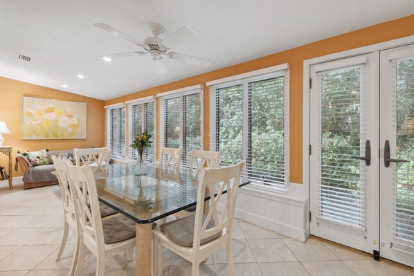 A dining area with a glass table, white chairs, and a ceiling fan.