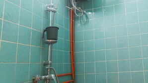Une salle de bain avec des carreaux de couleur turquoise, un lavabo blanc, des toilettes et une douche dotée d’un pommeau fixé au plafond, également de couleur blanche.