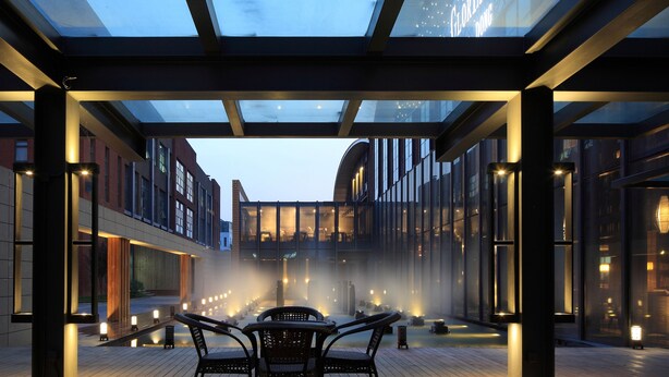 A modern indoor courtyard with a glass ceiling, seating areas, and a central water feature. - Gloria Plaza Hotel Dongsheng (Beijing)