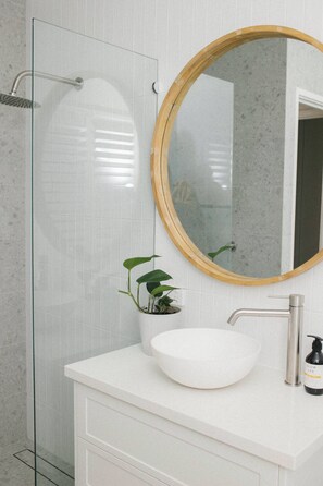 Bathroom features a glass-enclosed shower, white sink, and wooden-framed mirror.