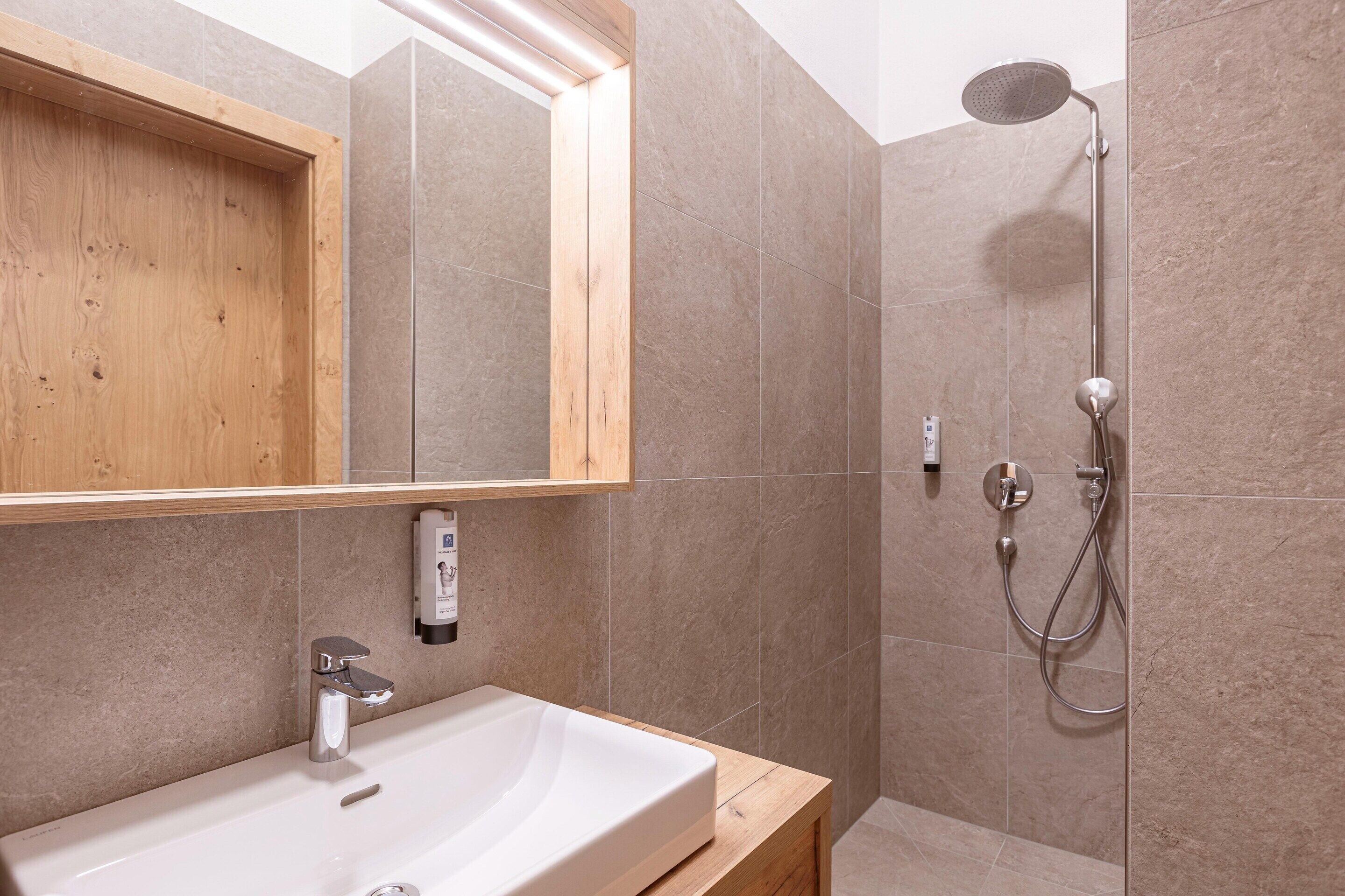 Un bagno con un mobile bagno in legno, un lavandino bianco, uno specchio e una doccia con soffione a mano.