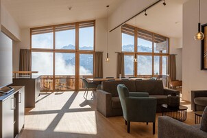 Amplia sala de estar con ventanas grandes, sofá, sillas, una mesa de comedor y zona de cocina.