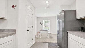 Een moderne keuken met witte kasten, een roestvrijstalen koelkast en een kleine eethoek met twee krukken.
