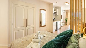 Une chambre avec un lit, un canapé vert, une cloison en bois et, au fond, un coin cuisine.