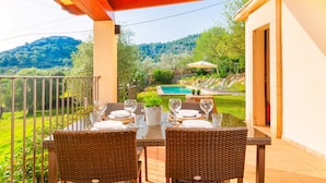 A dining area with wicker furniture and a view of a pool and garden. - CAN GARDO - Villa with private pool and Free Wifi (Pollença)
