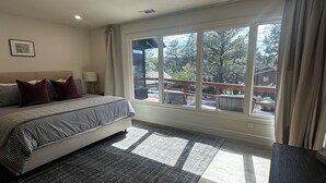 A bedroom with a large bed, a view of the outdoors, and a window with curtains.