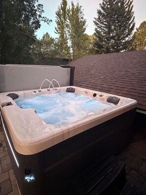 An outdoor hot tub with a built-in American flag, surrounded by trees and a brick wall.