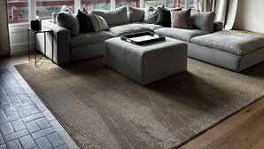 A modern living room with a sectional sofa, a coffee table, and a large window offering a view of the outdoors.