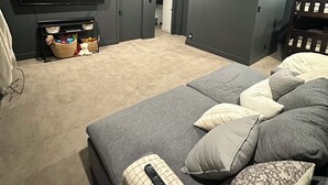 A modern living room with a large flat-screen TV, a sofa with cushions, and a fireplace.