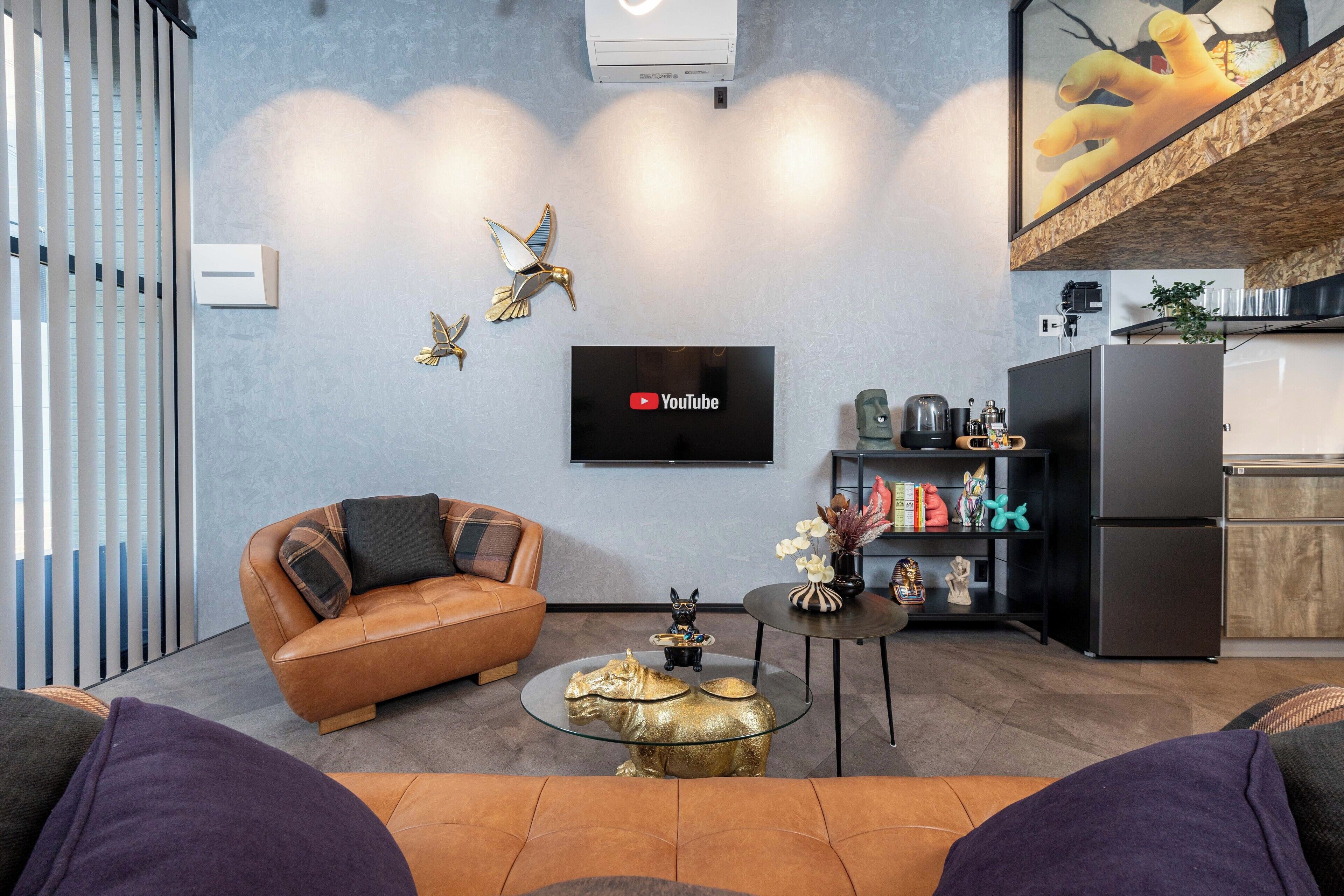 A modern living room with a leather sofa, a glass coffee table, and a flat-screen TV mounted on the wall.