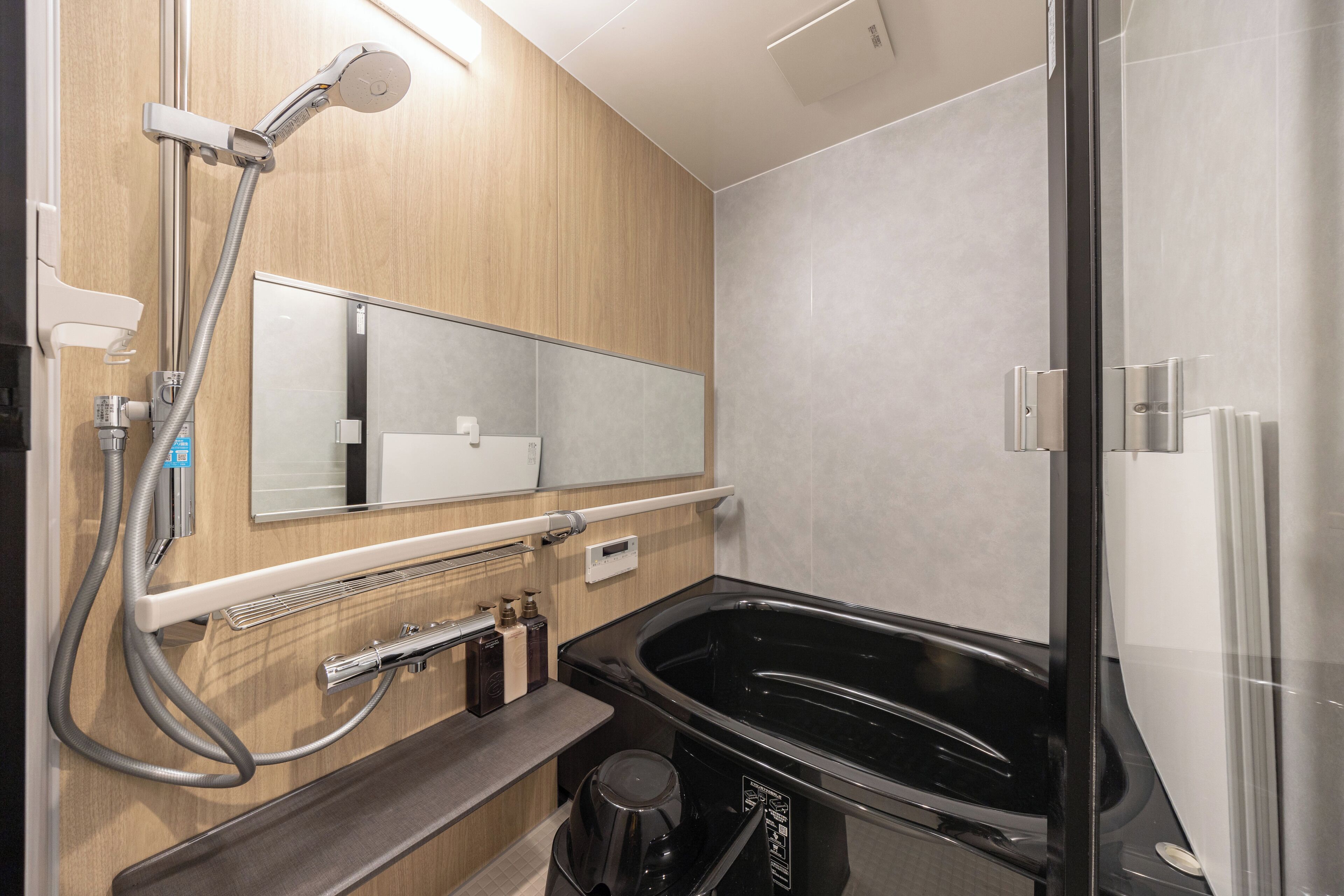 A modern bathroom with a glass shower enclosure, a black bathtub, and a wooden vanity.
