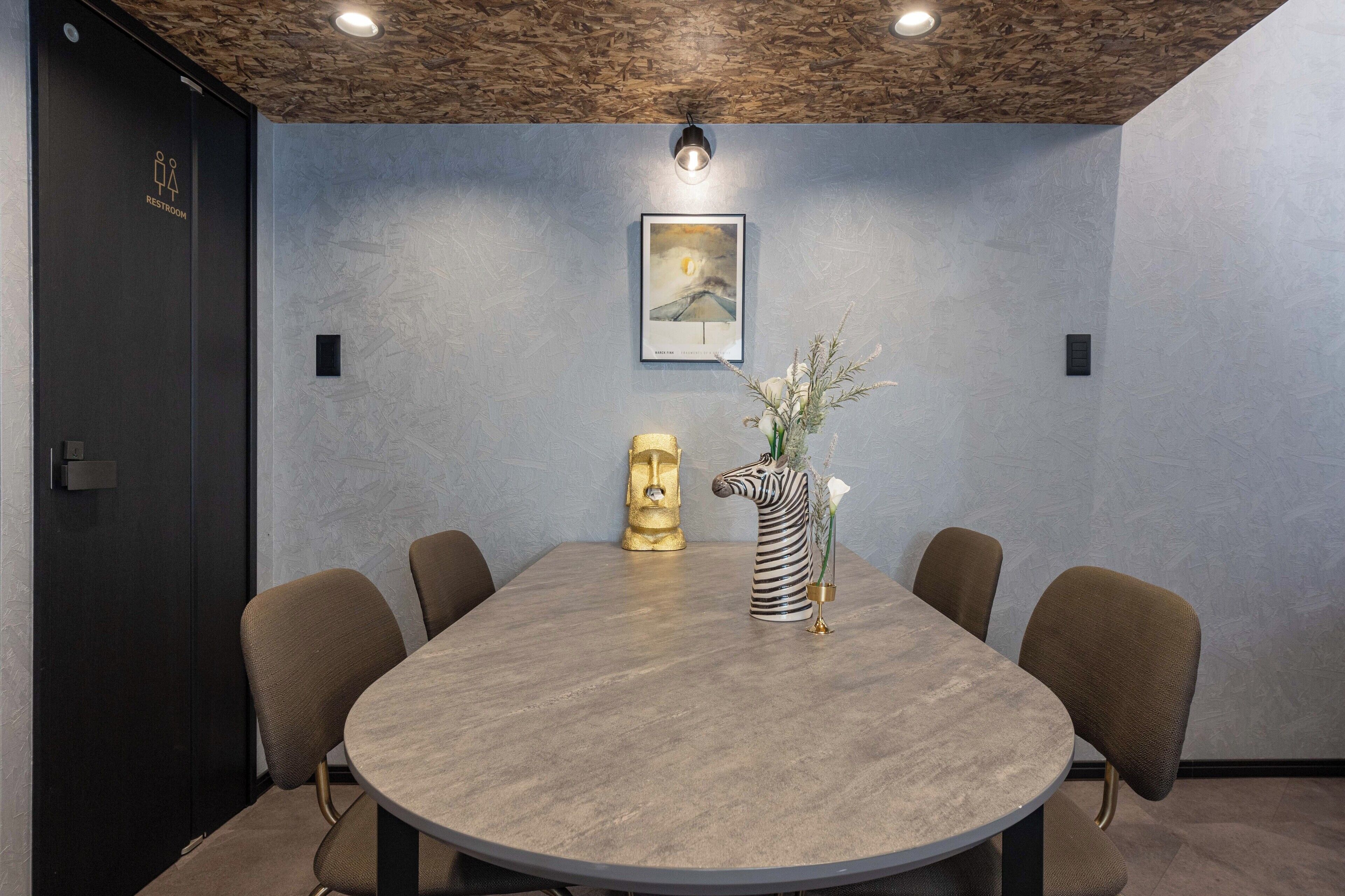 A conference room with a round table, six chairs, a zebra-striped vase with flowers, a golden statue, and a framed picture on the wall.